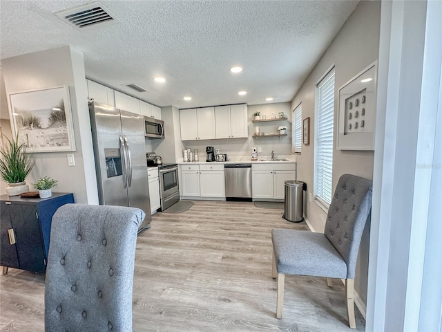 kitchen featuring appliances with stainless steel finishes, light wood-type flooring, a textured ceiling, sink, and white cabinets