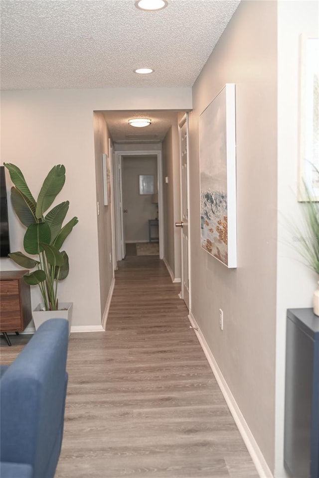 hall with a textured ceiling and light hardwood / wood-style flooring