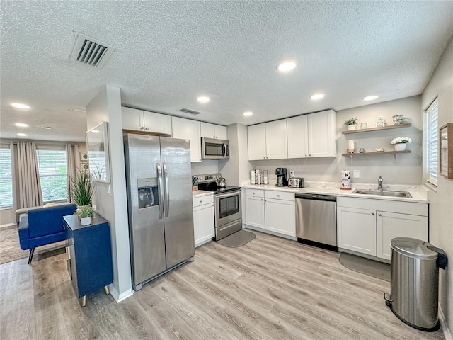 kitchen featuring white cabinetry, sink, light hardwood / wood-style floors, a textured ceiling, and appliances with stainless steel finishes