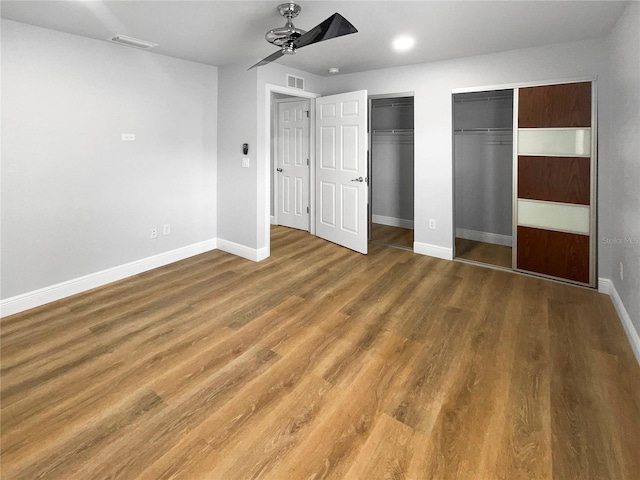 unfurnished bedroom with hardwood / wood-style floors, ceiling fan, and two closets