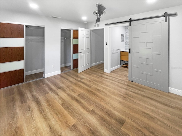 unfurnished bedroom featuring a barn door, ceiling fan, and light hardwood / wood-style flooring