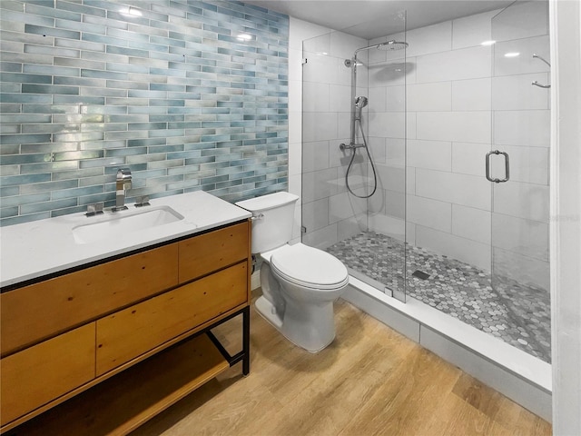 bathroom featuring toilet, hardwood / wood-style floors, vanity, backsplash, and a shower with shower door