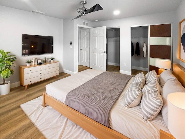 bedroom with hardwood / wood-style floors, ceiling fan, and two closets