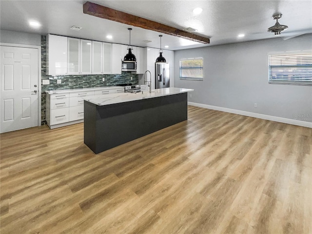 kitchen featuring white cabinetry, appliances with stainless steel finishes, beam ceiling, decorative light fixtures, and an island with sink