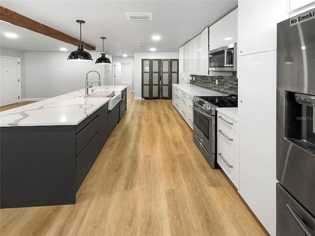 kitchen with light wood-type flooring, appliances with stainless steel finishes, a large island, pendant lighting, and white cabinets