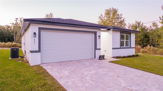 single story home featuring a lawn, a garage, and central air condition unit