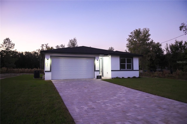 ranch-style home with a lawn, central AC unit, and a garage