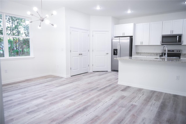 kitchen featuring white cabinets, light hardwood / wood-style flooring, appliances with stainless steel finishes, a notable chandelier, and light stone counters