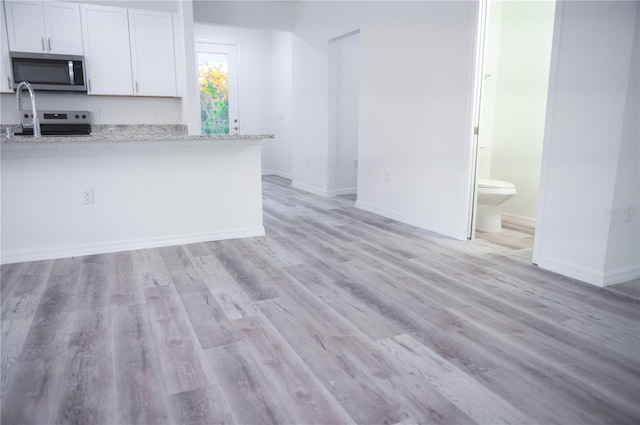 kitchen featuring light hardwood / wood-style floors, light stone counters, white cabinetry, and stainless steel appliances