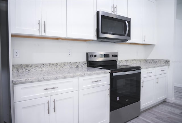 kitchen featuring white cabinets, appliances with stainless steel finishes, light wood-type flooring, and light stone countertops