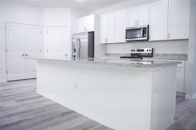 kitchen featuring light stone counters, stainless steel appliances, a kitchen island with sink, white cabinets, and light hardwood / wood-style floors