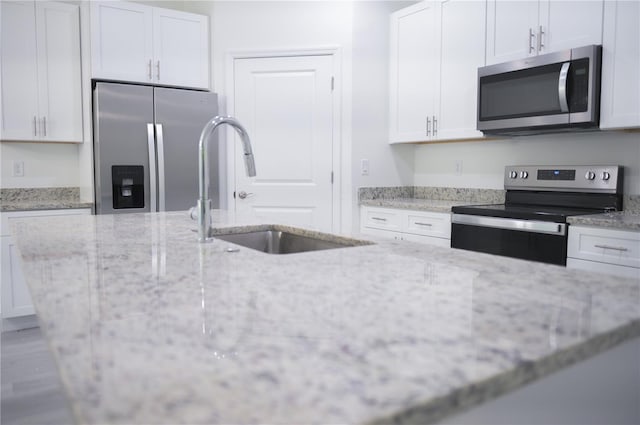 kitchen featuring light stone countertops, appliances with stainless steel finishes, white cabinetry, and sink