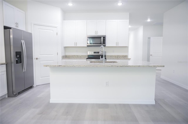 kitchen featuring appliances with stainless steel finishes, light stone counters, sink, white cabinets, and an island with sink