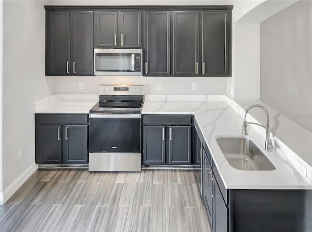 kitchen with stainless steel appliances, light hardwood / wood-style floors, sink, and light stone counters