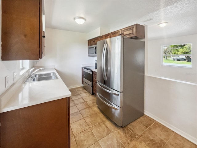 kitchen featuring appliances with stainless steel finishes, sink, light tile patterned floors, and a textured ceiling