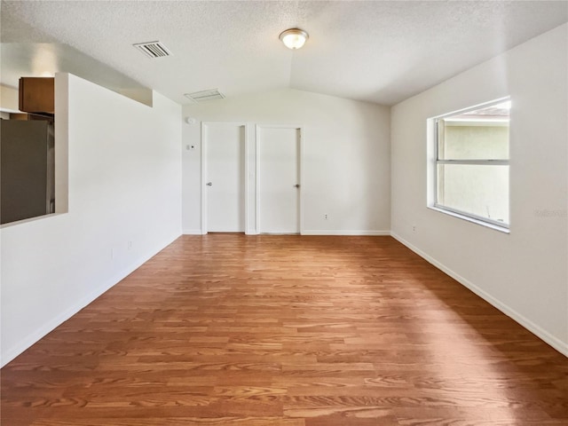 empty room featuring vaulted ceiling, hardwood / wood-style flooring, and a textured ceiling