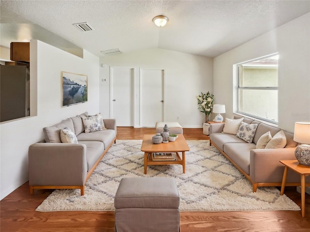 living room with light hardwood / wood-style floors, a textured ceiling, and vaulted ceiling