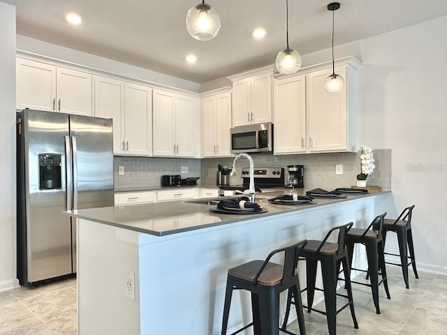 kitchen featuring pendant lighting, kitchen peninsula, backsplash, white cabinetry, and appliances with stainless steel finishes