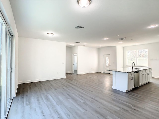 kitchen featuring a kitchen island with sink, sink, hardwood / wood-style floors, stainless steel dishwasher, and white cabinetry