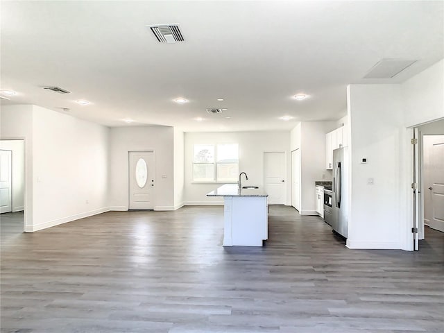 kitchen featuring dark wood-type flooring, an island with sink, stainless steel fridge, sink, and white cabinets