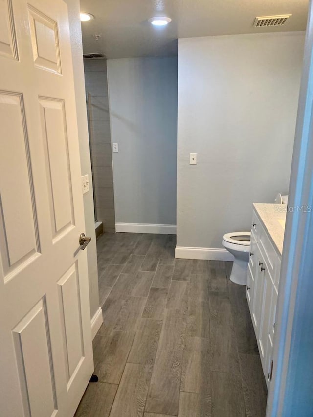 bathroom with hardwood / wood-style floors, vanity, toilet, and walk in shower