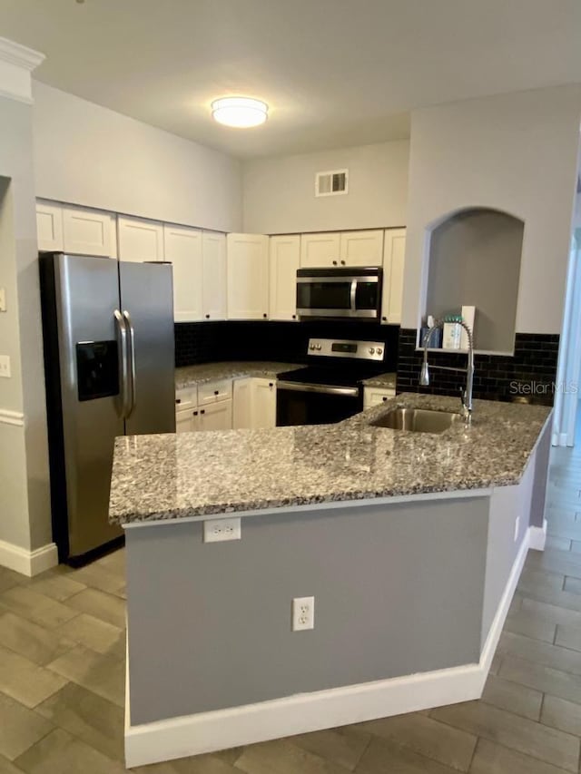 kitchen featuring white cabinets, light stone counters, kitchen peninsula, and appliances with stainless steel finishes