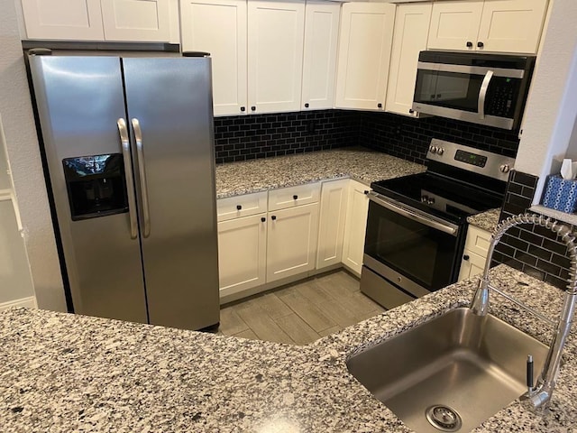 kitchen featuring white cabinets, stainless steel appliances, light hardwood / wood-style flooring, and tasteful backsplash