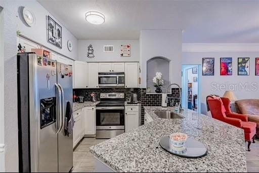 kitchen with white cabinets, sink, appliances with stainless steel finishes, tasteful backsplash, and light stone counters