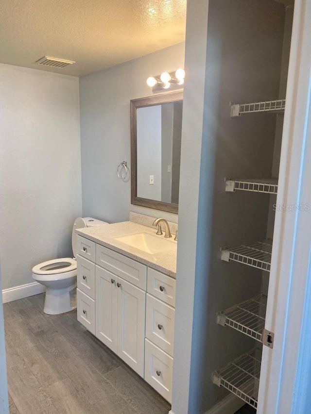 bathroom featuring hardwood / wood-style flooring, vanity, toilet, and a textured ceiling