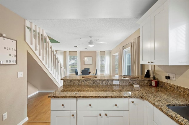 kitchen with white cabinets, light hardwood / wood-style floors, a textured ceiling, and stone countertops