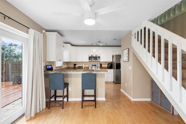 kitchen featuring stainless steel appliances, light wood-type flooring, white cabinetry, a breakfast bar area, and kitchen peninsula