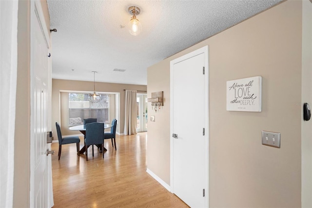 hall with a textured ceiling and light hardwood / wood-style floors