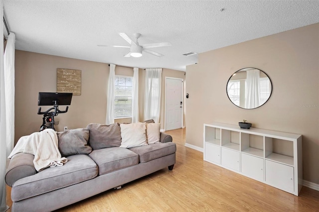 living room with light hardwood / wood-style floors, ceiling fan, and a textured ceiling