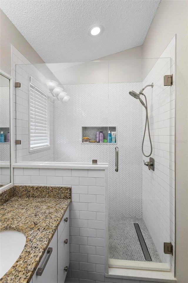 bathroom featuring walk in shower, vanity, a textured ceiling, and lofted ceiling