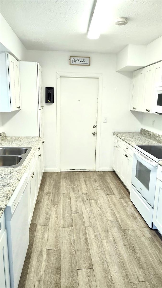 kitchen with white appliances, sink, light hardwood / wood-style floors, and white cabinets