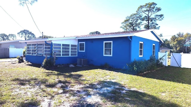 rear view of house with central AC unit and a lawn