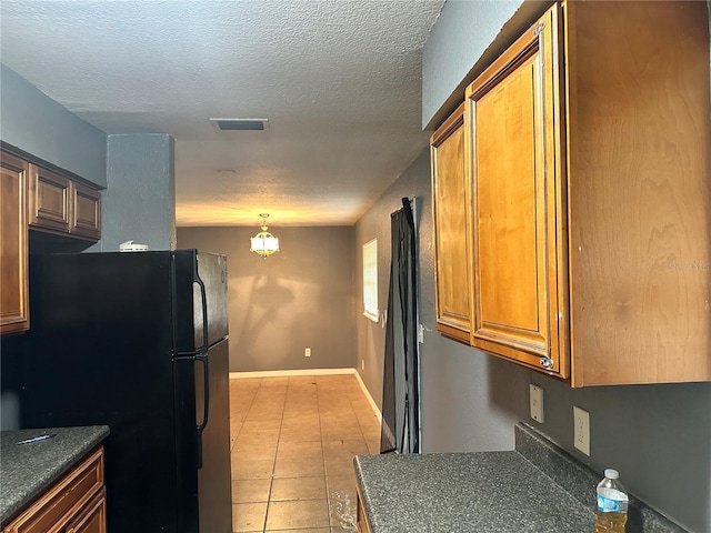 kitchen featuring black refrigerator, decorative light fixtures, a textured ceiling, and light tile patterned floors