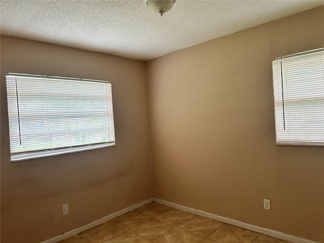 empty room with a wealth of natural light, a textured ceiling, and light tile patterned floors