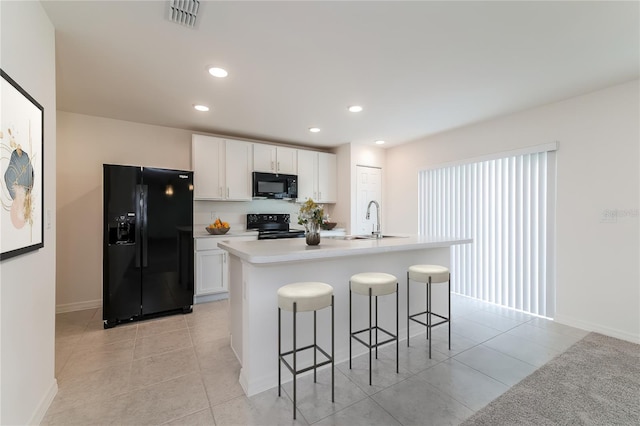 kitchen with a kitchen bar, black appliances, light tile patterned floors, an island with sink, and white cabinetry