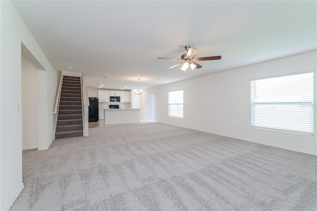 unfurnished living room with ceiling fan with notable chandelier and light colored carpet