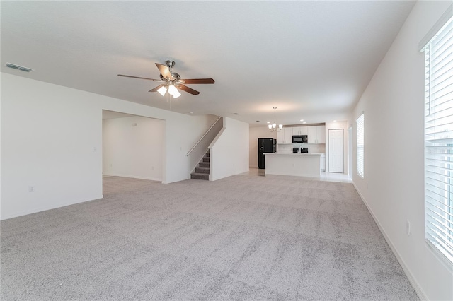 unfurnished living room featuring light colored carpet, a healthy amount of sunlight, and ceiling fan with notable chandelier