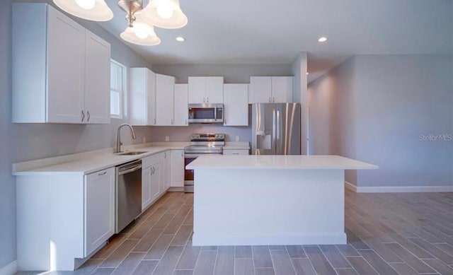 kitchen with stainless steel appliances, a kitchen island, sink, hardwood / wood-style floors, and white cabinets