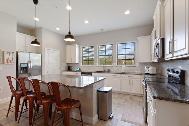 kitchen with stainless steel appliances, hanging light fixtures, sink, a kitchen island, and white cabinetry