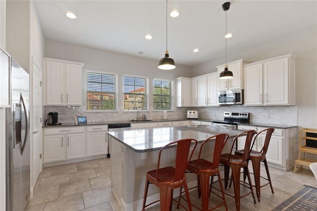 kitchen with white cabinets, hanging light fixtures, a kitchen island, and appliances with stainless steel finishes