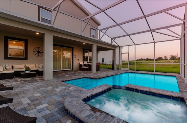 pool at dusk featuring outdoor lounge area, glass enclosure, a patio, and an in ground hot tub