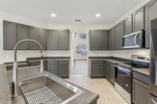 kitchen featuring sink, appliances with stainless steel finishes, a textured ceiling, light tile patterned floors, and gray cabinets