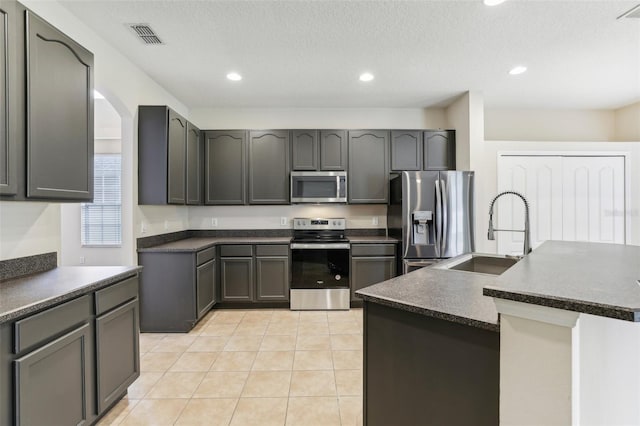 kitchen featuring stainless steel appliances, a center island with sink, sink, a textured ceiling, and light tile patterned floors