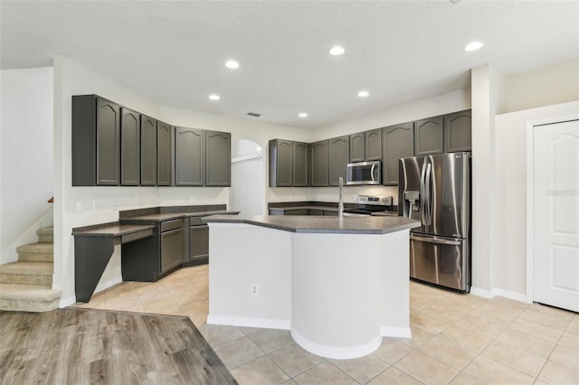 kitchen with appliances with stainless steel finishes, a textured ceiling, light tile patterned floors, sink, and an island with sink