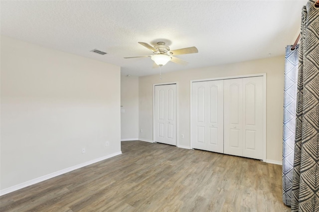 unfurnished bedroom featuring light hardwood / wood-style floors, ceiling fan, a textured ceiling, and two closets