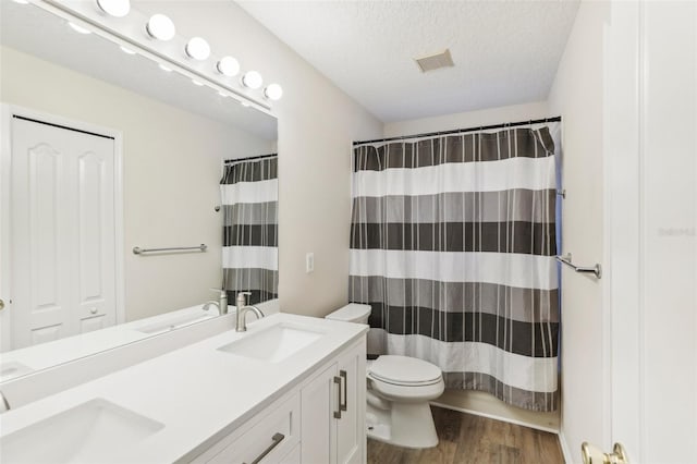 bathroom with hardwood / wood-style flooring, a textured ceiling, curtained shower, vanity, and toilet